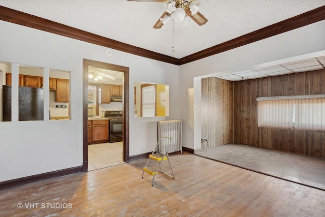 empty room featuring radiator, light hardwood / wood-style flooring, wood walls, a textured ceiling, and ornamental molding