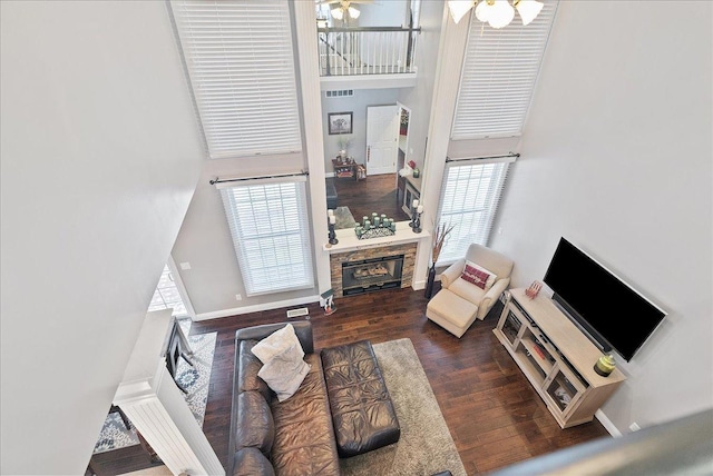 living room with a high ceiling, dark hardwood / wood-style floors, a stone fireplace, and a healthy amount of sunlight