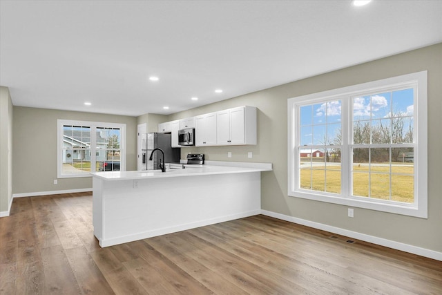 kitchen with sink, light hardwood / wood-style flooring, stainless steel appliances, white cabinets, and kitchen peninsula