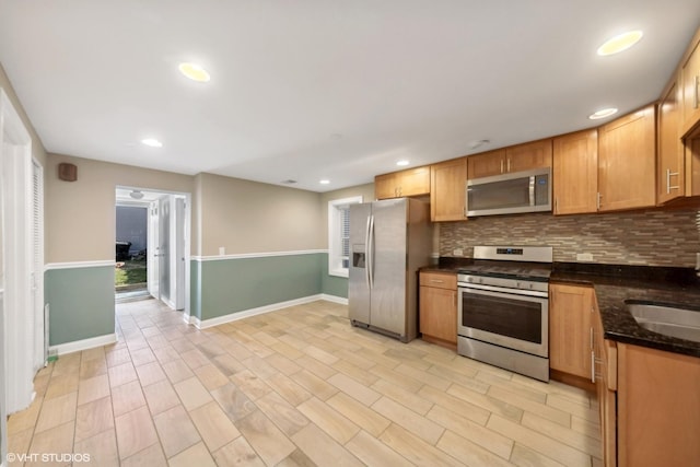 kitchen featuring decorative backsplash, dark stone counters, stainless steel appliances, sink, and light hardwood / wood-style flooring