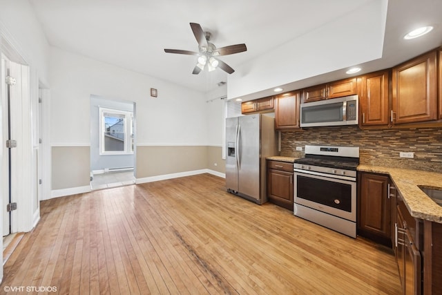 kitchen featuring light stone countertops, appliances with stainless steel finishes, decorative backsplash, baseboard heating, and light hardwood / wood-style flooring