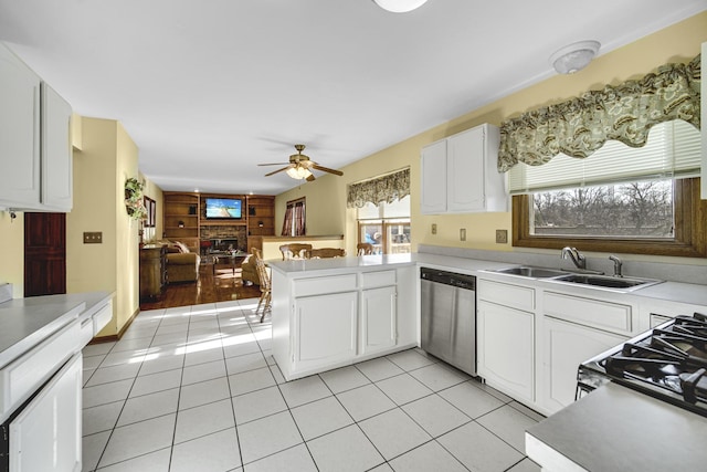 kitchen with sink, a brick fireplace, stainless steel dishwasher, kitchen peninsula, and white cabinets