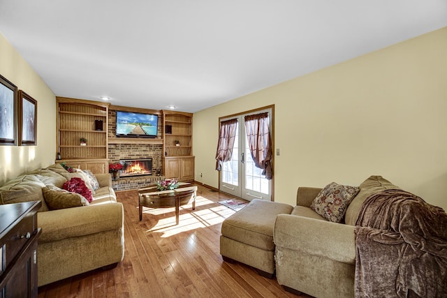 living room featuring a brick fireplace, light wood-type flooring, french doors, and built in features