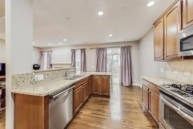 kitchen with kitchen peninsula, appliances with stainless steel finishes, tasteful backsplash, dark wood-type flooring, and sink