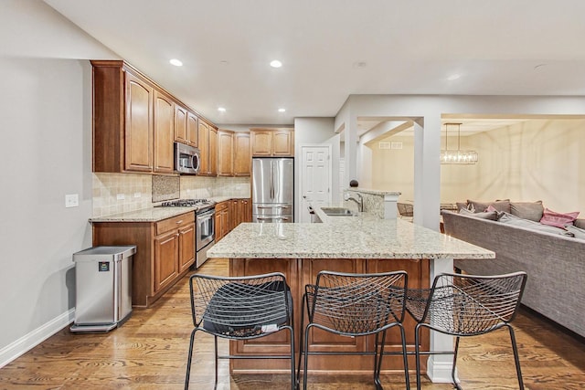 kitchen featuring a kitchen breakfast bar, backsplash, stainless steel appliances, sink, and light hardwood / wood-style flooring