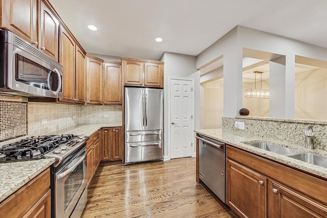 kitchen with a chandelier, appliances with stainless steel finishes, light stone counters, and dark wood-type flooring