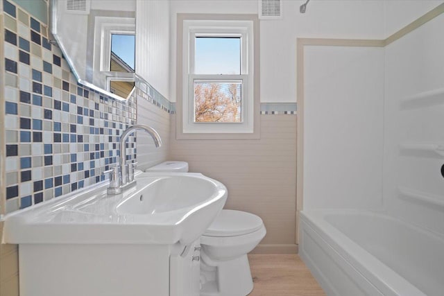 bathroom with hardwood / wood-style floors, a bathtub, toilet, and tile walls