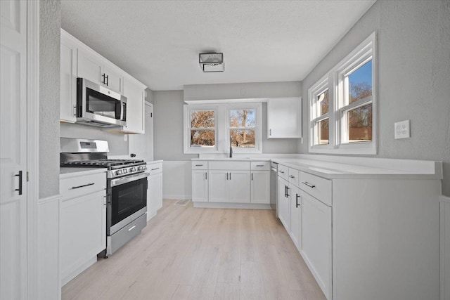 kitchen featuring a textured ceiling, light wood-type flooring, white cabinetry, and stainless steel appliances