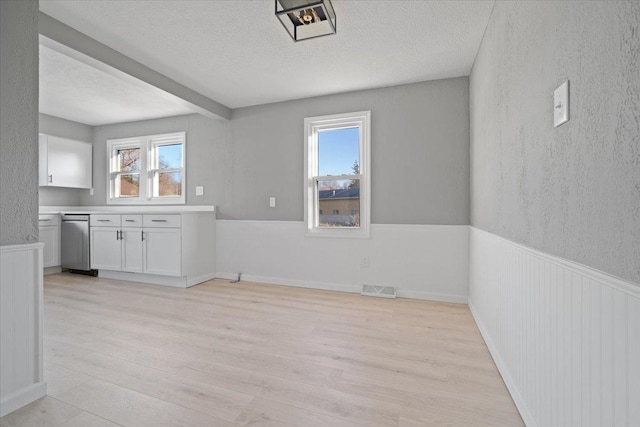 unfurnished dining area featuring a textured ceiling, light wood-type flooring, and plenty of natural light