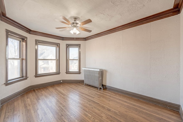 unfurnished room with plenty of natural light, ceiling fan, wood-type flooring, and radiator heating unit