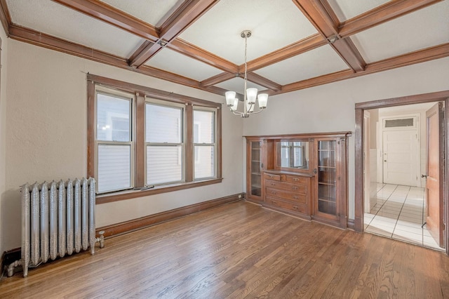 unfurnished dining area with hardwood / wood-style floors, an inviting chandelier, coffered ceiling, beamed ceiling, and radiator heating unit