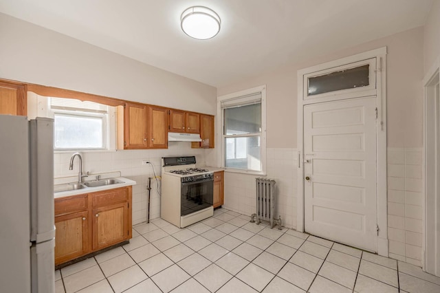 kitchen with radiator, sink, white appliances, light tile patterned flooring, and tile walls