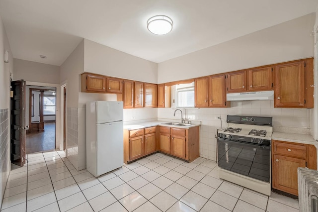 kitchen featuring white appliances, sink, light tile patterned floors, and tile walls