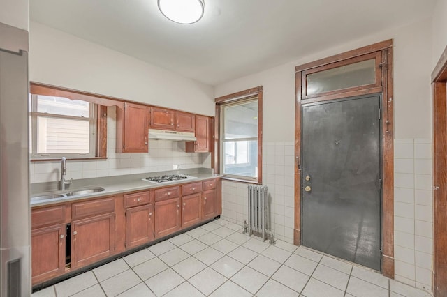 kitchen featuring radiator, stainless steel gas cooktop, sink, light tile patterned floors, and tile walls