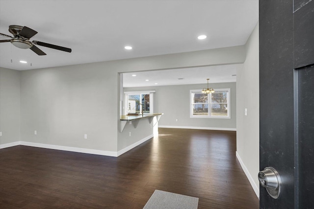 unfurnished living room featuring ceiling fan with notable chandelier and dark wood-type flooring