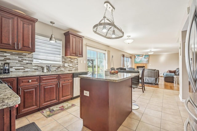 kitchen featuring light stone countertops, appliances with stainless steel finishes, light tile patterned floors, a kitchen island, and hanging light fixtures