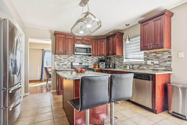 kitchen featuring a center island, stainless steel appliances, light stone counters, and hanging light fixtures