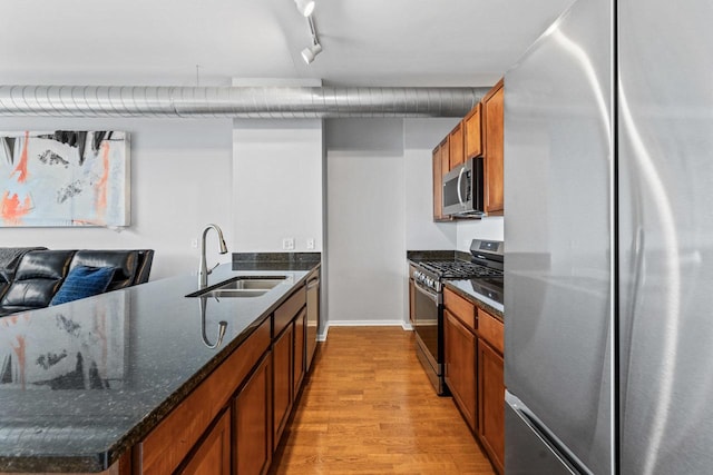 kitchen featuring sink, dark stone countertops, track lighting, appliances with stainless steel finishes, and light wood-type flooring