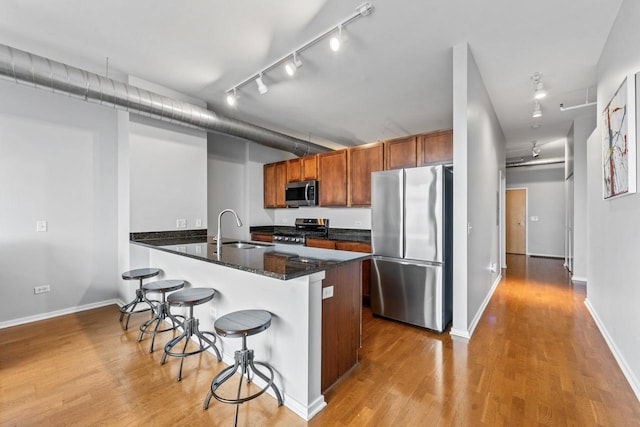 kitchen with kitchen peninsula, light wood-type flooring, stainless steel appliances, sink, and a breakfast bar area