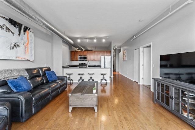 living room with track lighting, light hardwood / wood-style flooring, and sink