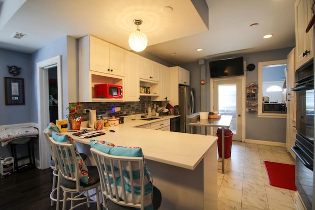 kitchen with kitchen peninsula, backsplash, white cabinetry, hanging light fixtures, and a breakfast bar area