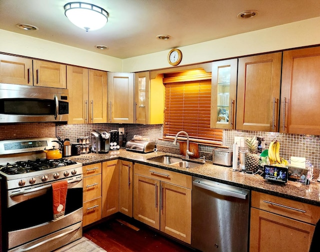 kitchen with backsplash, dark wood-type flooring, dark stone counters, sink, and appliances with stainless steel finishes