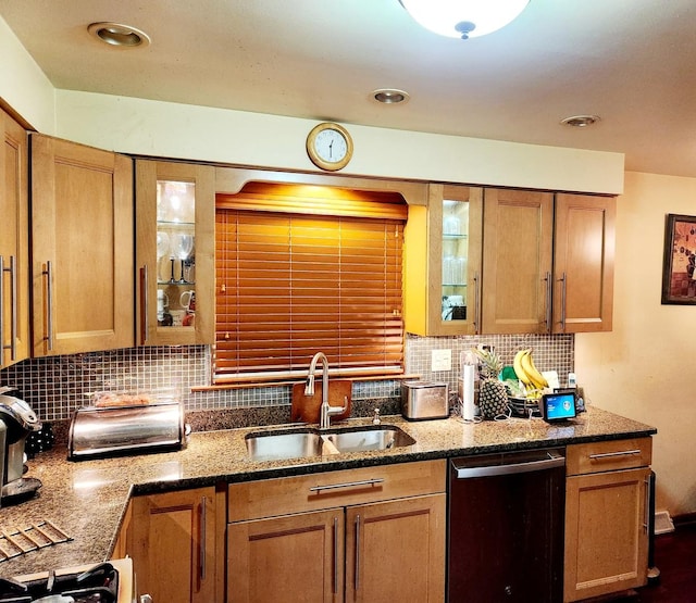 kitchen with stainless steel dishwasher, dark stone countertops, sink, and tasteful backsplash