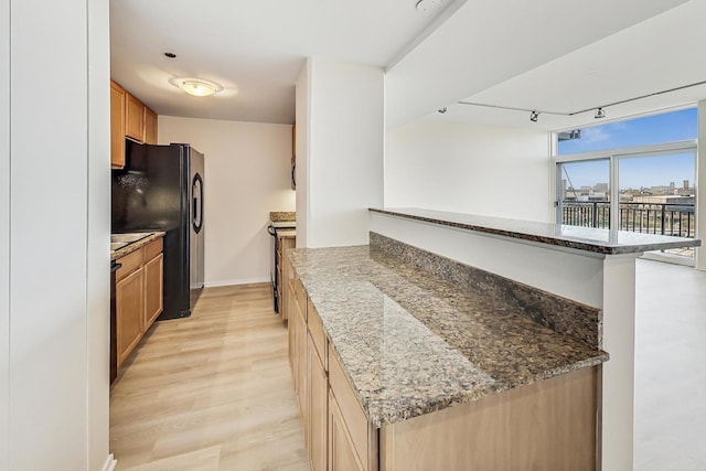 kitchen with black refrigerator, kitchen peninsula, rail lighting, light hardwood / wood-style flooring, and dark stone countertops