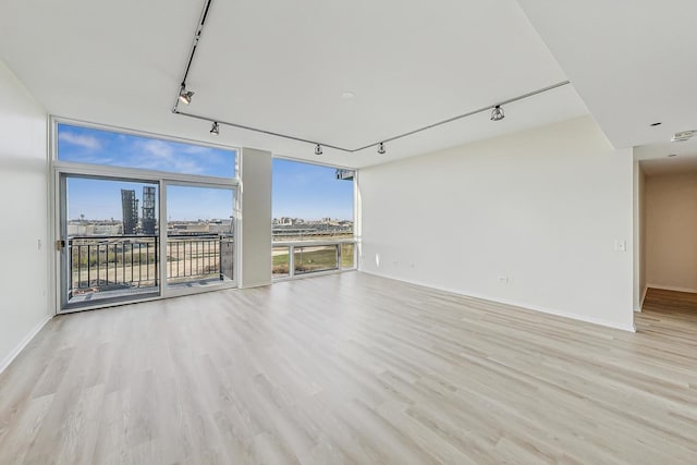 empty room featuring light hardwood / wood-style flooring, track lighting, and a wall of windows