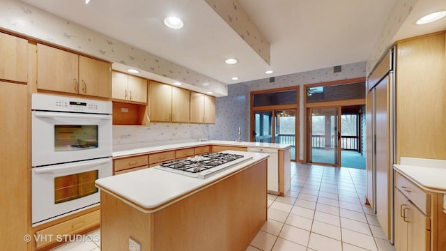 kitchen featuring light brown cabinets, a kitchen island, light tile patterned flooring, and appliances with stainless steel finishes