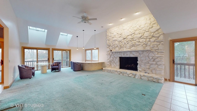 unfurnished living room with ceiling fan, a stone fireplace, light tile patterned floors, and a wealth of natural light