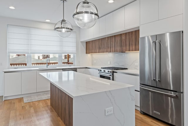 kitchen featuring high end appliances, decorative light fixtures, white cabinetry, and a kitchen island