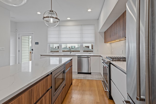 kitchen with decorative light fixtures, white cabinets, light stone counters, stainless steel appliances, and light wood-type flooring