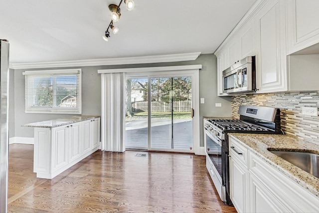 kitchen featuring hardwood / wood-style flooring, a healthy amount of sunlight, white cabinetry, and stainless steel appliances