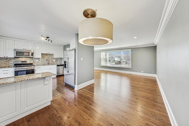 kitchen with white cabinetry, stainless steel appliances, light stone counters, dark hardwood / wood-style flooring, and ornamental molding