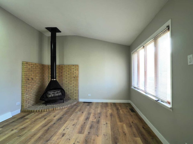 unfurnished living room with a wood stove, vaulted ceiling, and hardwood / wood-style flooring