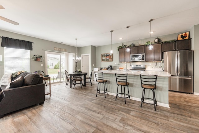 kitchen with a kitchen island with sink, light wood-type flooring, appliances with stainless steel finishes, dark brown cabinets, and a breakfast bar area