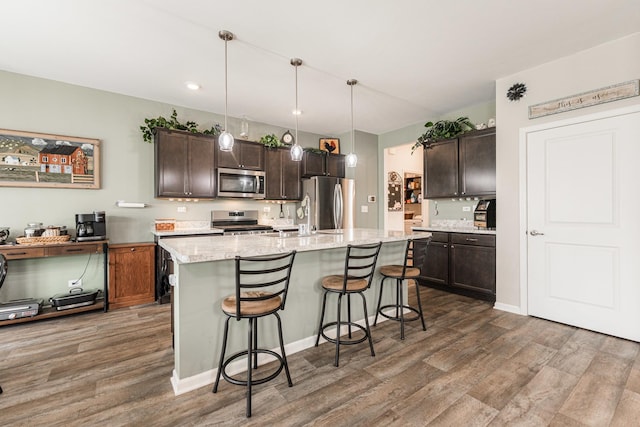 kitchen with pendant lighting, dark brown cabinets, stainless steel appliances, and a kitchen island with sink