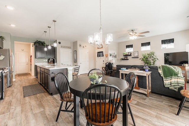 dining space featuring ceiling fan with notable chandelier, light hardwood / wood-style floors, and sink