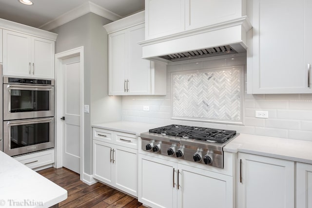 kitchen featuring backsplash, dark wood-type flooring, white cabinets, appliances with stainless steel finishes, and custom range hood