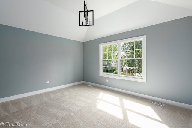 spare room with carpet, a chandelier, and vaulted ceiling