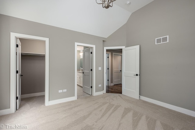 unfurnished bedroom featuring high vaulted ceiling, ensuite bath, a spacious closet, light colored carpet, and a closet