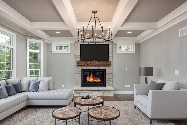 living room featuring beam ceiling, coffered ceiling, an inviting chandelier, a stone fireplace, and hardwood / wood-style floors