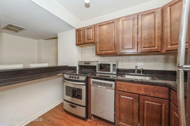 kitchen with sink, tasteful backsplash, dark stone countertops, appliances with stainless steel finishes, and hardwood / wood-style floors