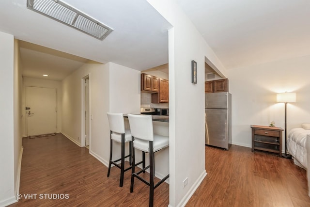 kitchen featuring dark wood-type flooring, a kitchen bar, stainless steel fridge, and backsplash