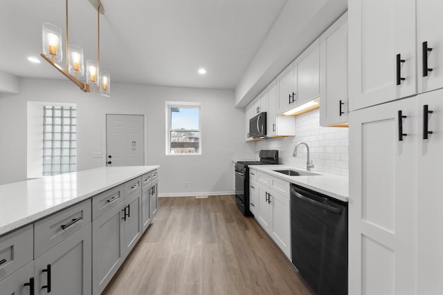 kitchen featuring pendant lighting, black appliances, sink, light wood-type flooring, and white cabinetry