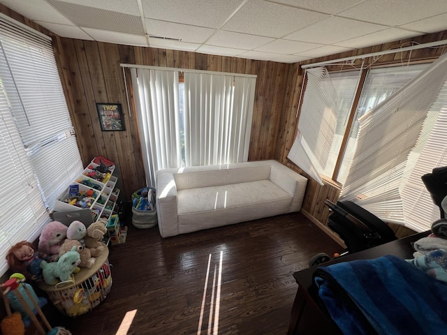 living room featuring dark hardwood / wood-style floors, a drop ceiling, and wood walls