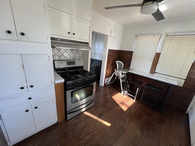 kitchen with dark wood-type flooring, stainless steel gas range, decorative backsplash, white cabinets, and ornamental molding