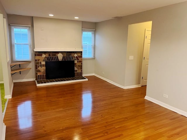 living room featuring a healthy amount of sunlight, a stone fireplace, and wood-type flooring