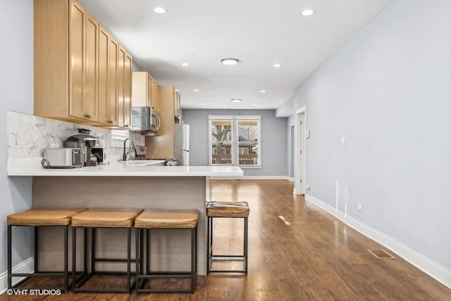 kitchen featuring light brown cabinets, dark hardwood / wood-style flooring, kitchen peninsula, a kitchen bar, and appliances with stainless steel finishes